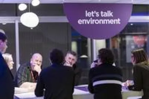 Des personnes assises à des tables dans une salle avec une pancarte indiquant "Discutons de l'environnement".