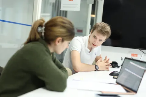 Dans une bureau, une femme et un homme discutent devants leurs ordinateurs