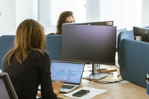 Deux femmes assises à leurs bureaux respectifs travaillant devant l'ordinateur.