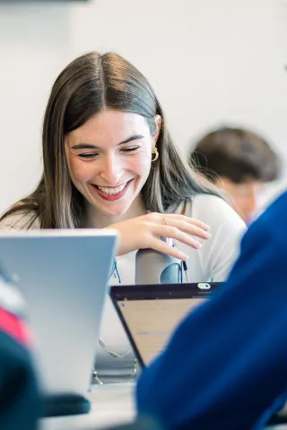Discussion en groupe avec une participante tenant un stylo, entourée d'ordinateurs portables, dans un environnement de travail dynamique.