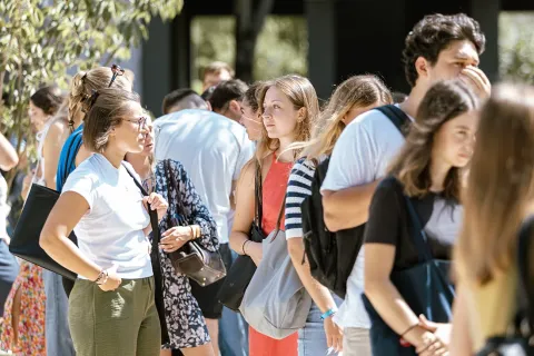 Group of emlyon students gathered outdoors on campus, talking and moving around in a sunny and lively area. 