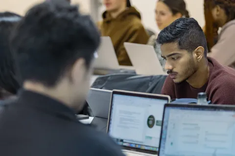Un groupe d'étudiants concentrés sur leur travail dans un cadre académique, entourés de plusieurs ordinateurs portables. On peut voir des documents ouverts à l'écran, soulignant l'ambiance de collaboration et d'apprentissage. Les étudiants semblent engagés dans leur tâche, favorisant un environnement d'étude actif.