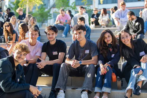 Group of students sitting on outdoor steps at the emlyon business school campus during a student life moment.