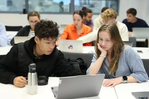 Étudiants travaillant ensemble sur un ordinateur portable dans une salle de classe moderne durant une session académique.