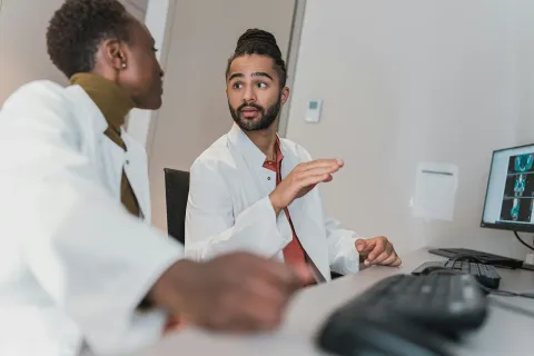 Two individuals in lab coats reviewing medical images or data displayed on a computer screen in a scientific workspace