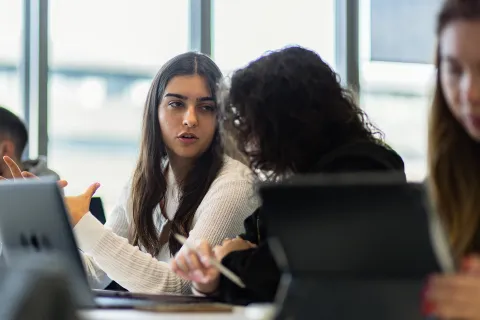 Personnes échangeant et travaillant ensemble autour d’un ordinateur et d’une tablette dans une salle de cours lumineuse