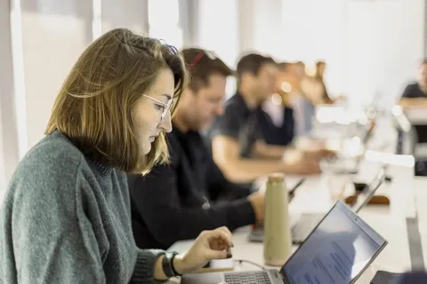 emlyon participants working on their laptops during a training session, seated along a large table in a classroom environment.