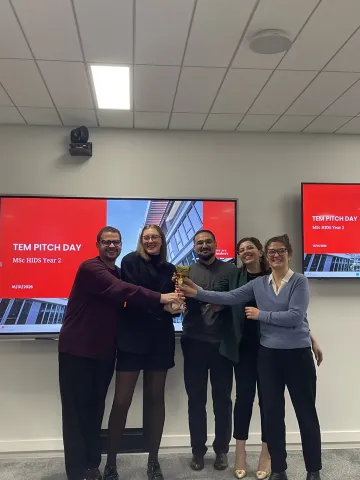 Étudiants du MSc in Healthcare Innovation & Data Science lors du TEM Pitch Day, présentant leur trophée devant les écrans de l’événement.