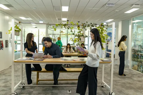 Students collaborating in an indoor workspace at emlyon business school with tables and informational materials.