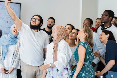 Groupe de personnes réunies dans une salle, regardant un smartphone tenu en hauteur par l’une d’elles