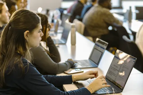 Students seated in a lecture room, using laptops side by side during a class session.