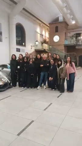  Groupe de personnes posant ensemble dans un vaste espace intérieur d’exposition, à proximité d’un véhicule exposé, avec une architecture moderne et des éléments muséographiques visibles, dans un contexte de visite éducative et de découverte.