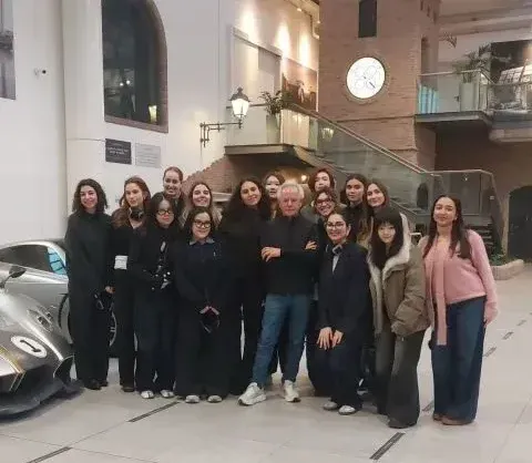 Group of people posing together in a large indoor exhibition space, near a vehicle on display, with modern architecture and exhibition elements visible, in an educational visit context.