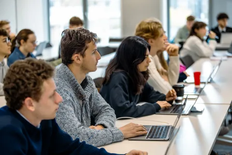 Students seated in a classroom, working on laptops during a course session.