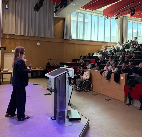 Audience attending a presentation in the modern emlyon hall, with a central screen and speakers on stage.