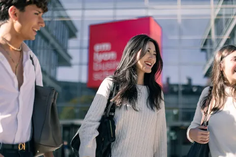 Étudiants d’emlyon marchant et discutant ensemble sur le campus de Lyon, avec des bâtiments académiques visibles en arrière-plan.