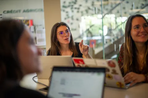 Des personnes travaillent autour d’une table avec des ordinateurs portables dans un espace académique moderne, lors d’une séance de travail collaboratif.