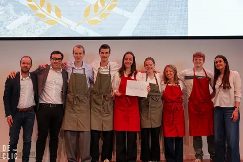 A group of students and supervisors pose together on a stage, some wearing aprons, with a person holding a document in the center. 