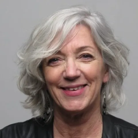 Portrait photographique d’une personne cadrée en buste, avec des cheveux courts et clairs, portant une veste sombre, sur un fond uni gris.
