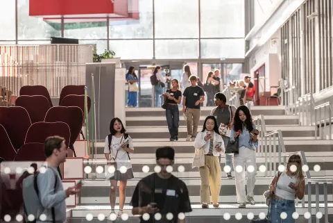 Étudiants circulant dans un hall de campus moderne avec escaliers et espaces de travail collaboratif