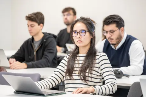 Étudiants en cours travaillant sur ordinateurs portables dans une salle de classe en école de management