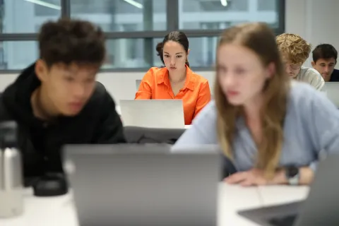 Étudiants travaillant sur des ordinateurs portables en salle de classe, avec une personne nette au centre et d’autres floues au premier plan et à l’arrière-plan