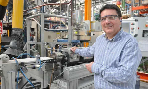 Une personne se tient devant un équipement industriel dans un atelier de production, entourée de machines et de structures métalliques.