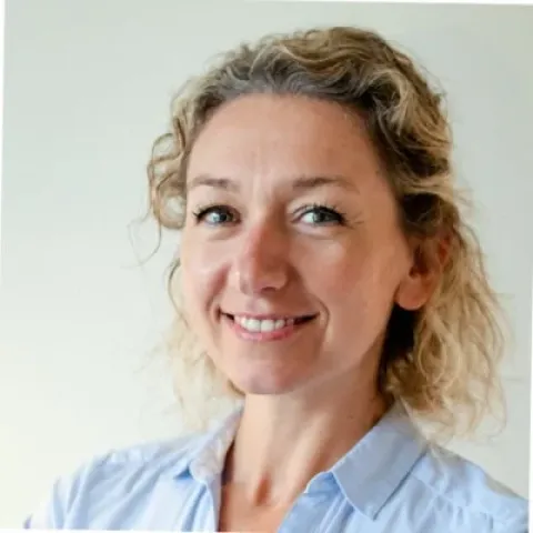 Portrait d’une personne aux cheveux ondulés portant une chemise bleu clair, devant un fond uni clair.