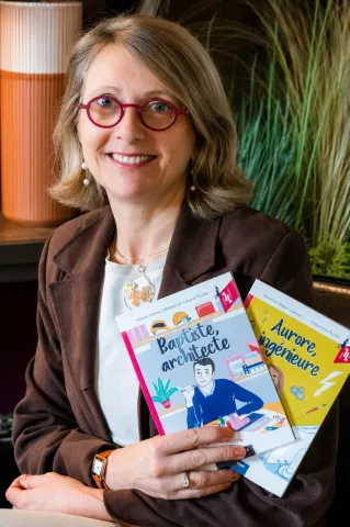 Une personne portant des lunettes est assise dans un intérieur et tient deux livres illustrés intitulés « Baptiste, architecte » et « Aurore, ingénieure ».
