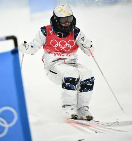 Personne équipée de skis, d’un casque et de bâtons, en action sur une piste enneigée lors d’une compétition de ski acrobatique.