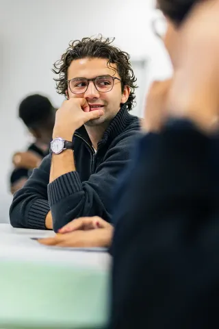 Business school students participating in a class while working on laptops and tablets in a modern learning environment.