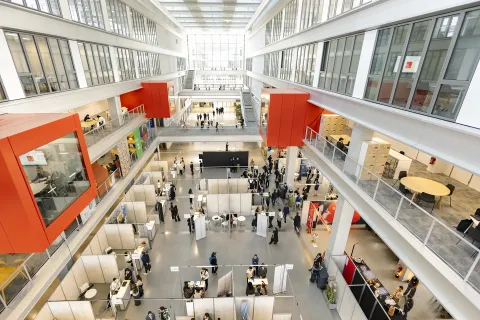 Atrium lumineux d’un campus avec espaces de travail, stands et visiteurs répartis sur plusieurs niveaux
