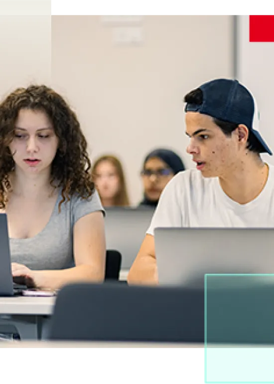Two students working on laptops in a classroom.