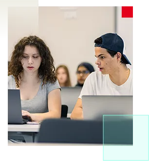 Two students working on laptops in a classroom.
